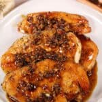 Three pieces covered in a dark, seasoned sauce reminiscent of Baked utensils and a garlic bulb in the background.
