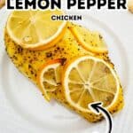 A piece of Baked Lemon Pepper Chicken, topped with fresh lemon slices on a white plate, with text overlay highlighting it as "Baked Lemon Pepper Chicken" and "tender.