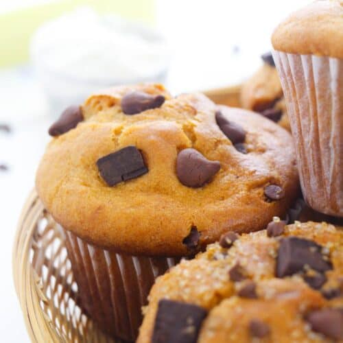 Close-up of bakery style chocolate chip muffins in a wicker basket, with visible chunks of chocolate and a blurred background.
