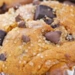 Close-up of a bakery style chocolate chip muffin with coarse sugar crystals on top, baked in a white paper liner.