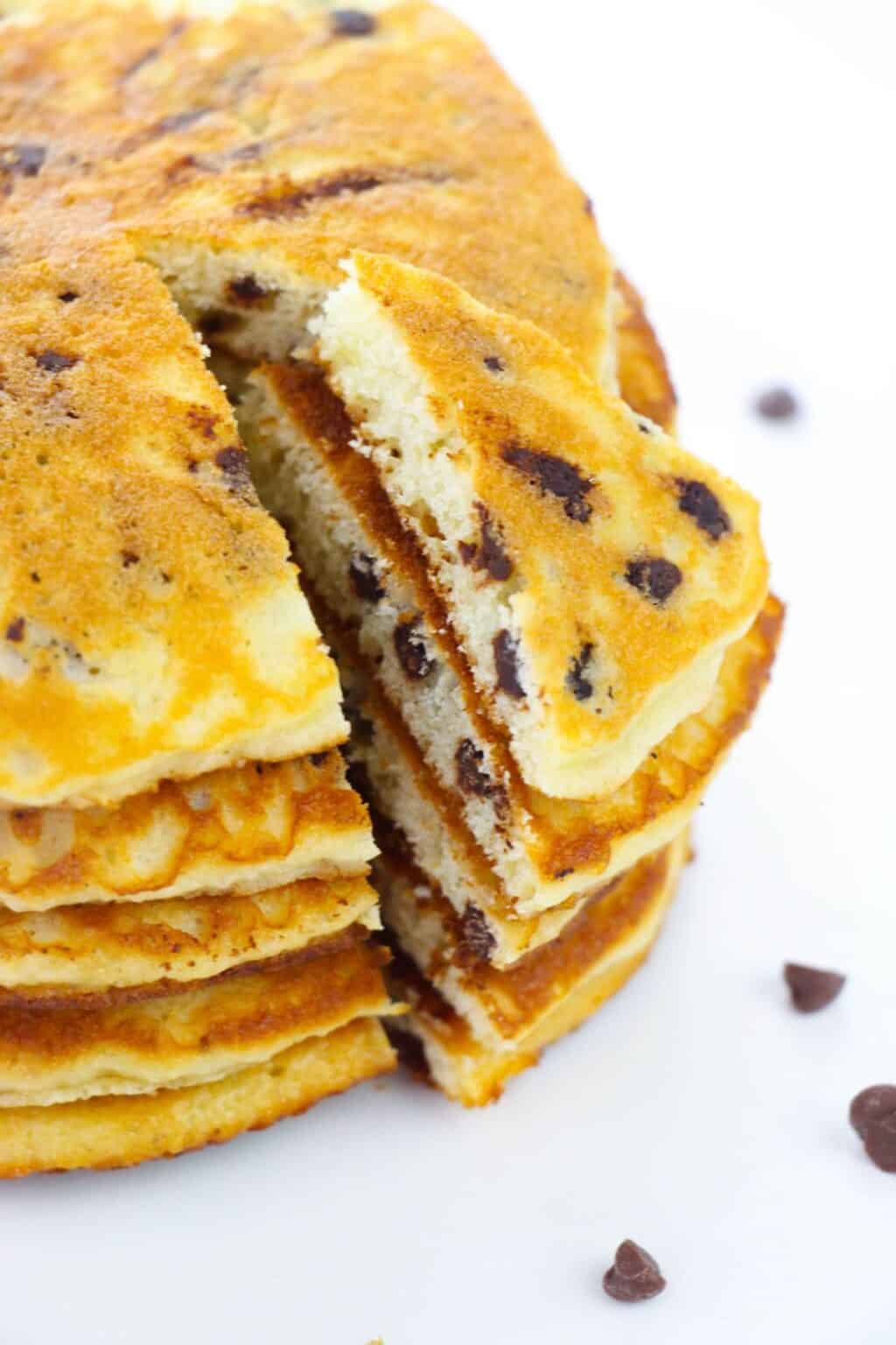 A stack of Cake Mix Pancakes with chocolate chips, one triangular slice partially removed to reveal the fluffy interior and gooey melted chocolate chips.