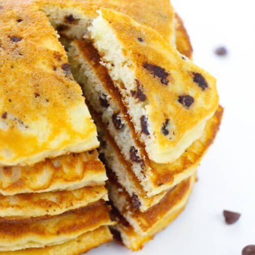 A stack of Cake Mix Pancakes with chocolate chips, one triangular slice partially removed to reveal the fluffy interior and gooey melted chocolate chips.