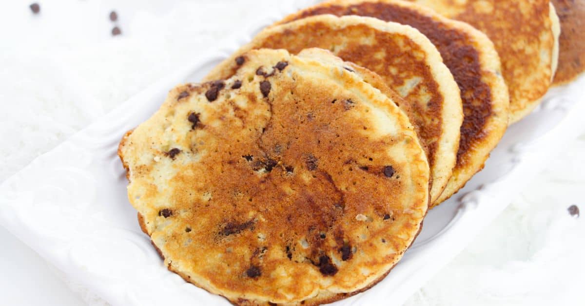 Four fluffy Cake Mix Pancakes studded with chocolate chips are stacked on a white rectangular plate.