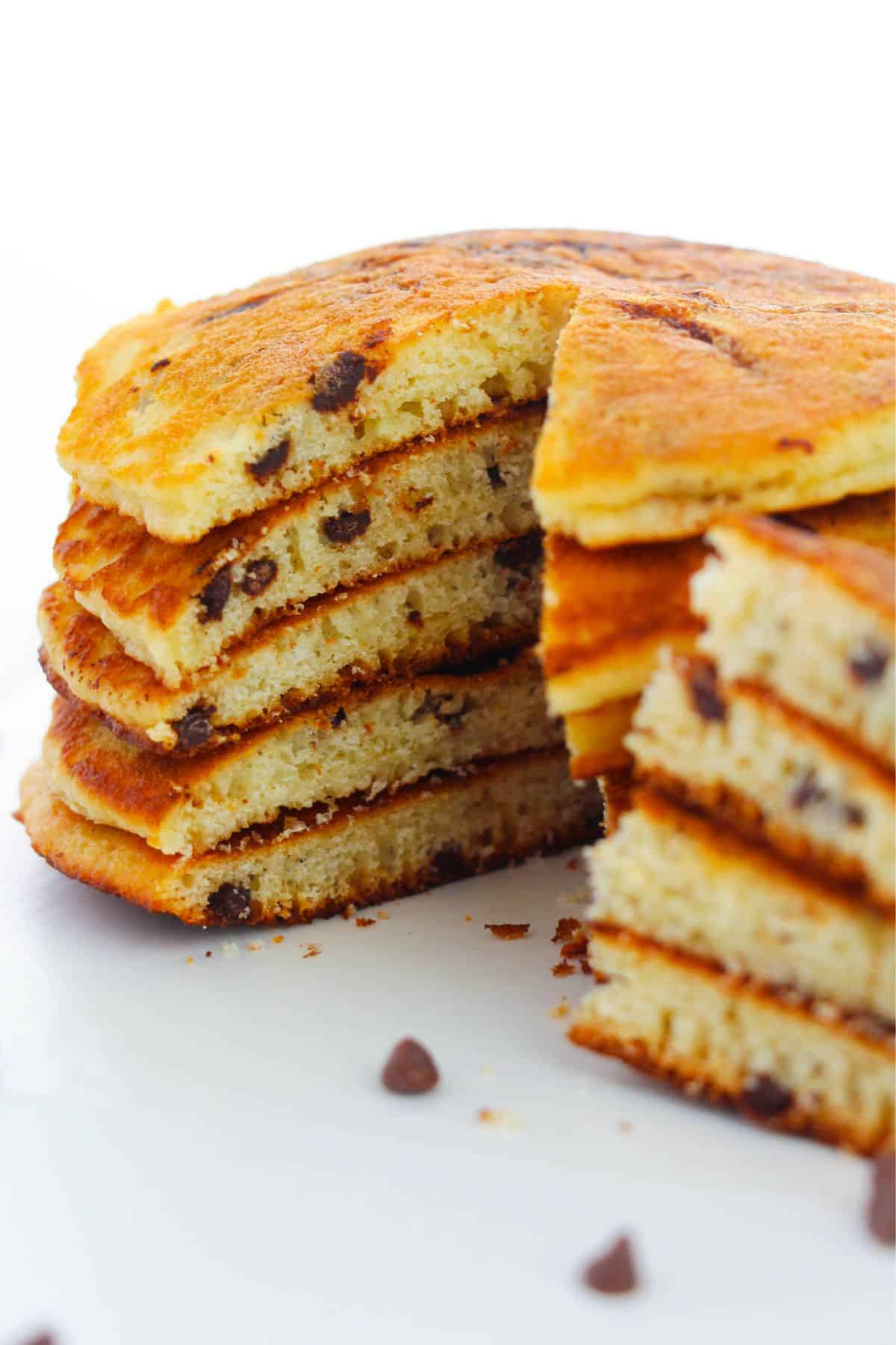 A stack of Cake Mix Pancakes with a wedge cut out, showing the fluffy inside texture and chocolate chips, sits on a white surface.