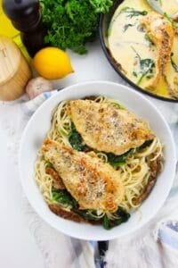 A bowl of Chicken cutlets.lemon, and herbs in the background.