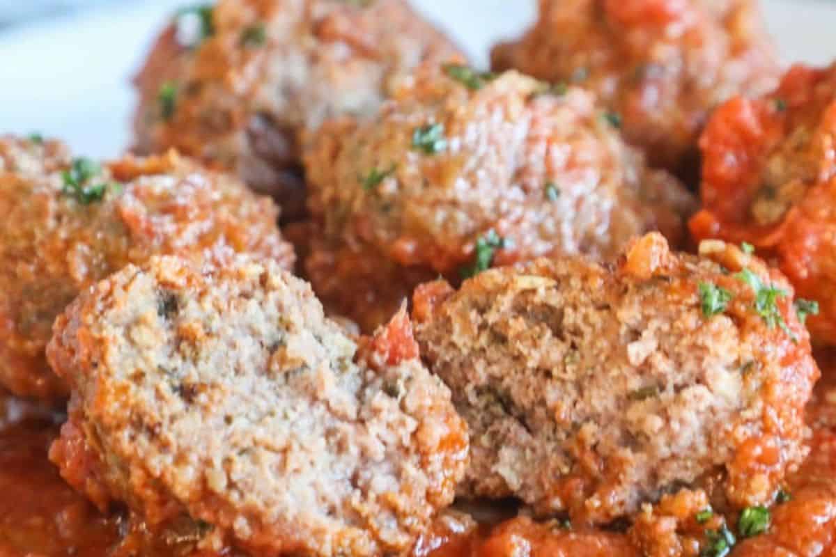 A close-up of several meatballs topped with tomato sauce and herbs, with one meatball cut open to show the inside texture—perfect for easy new mom freezer meals.