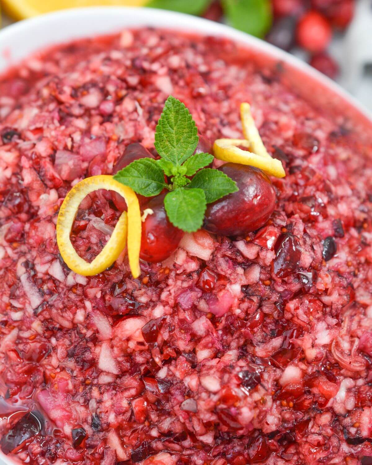 Close up shot of fresh cranberry sauce with oranges with mint and orange zest garnish.