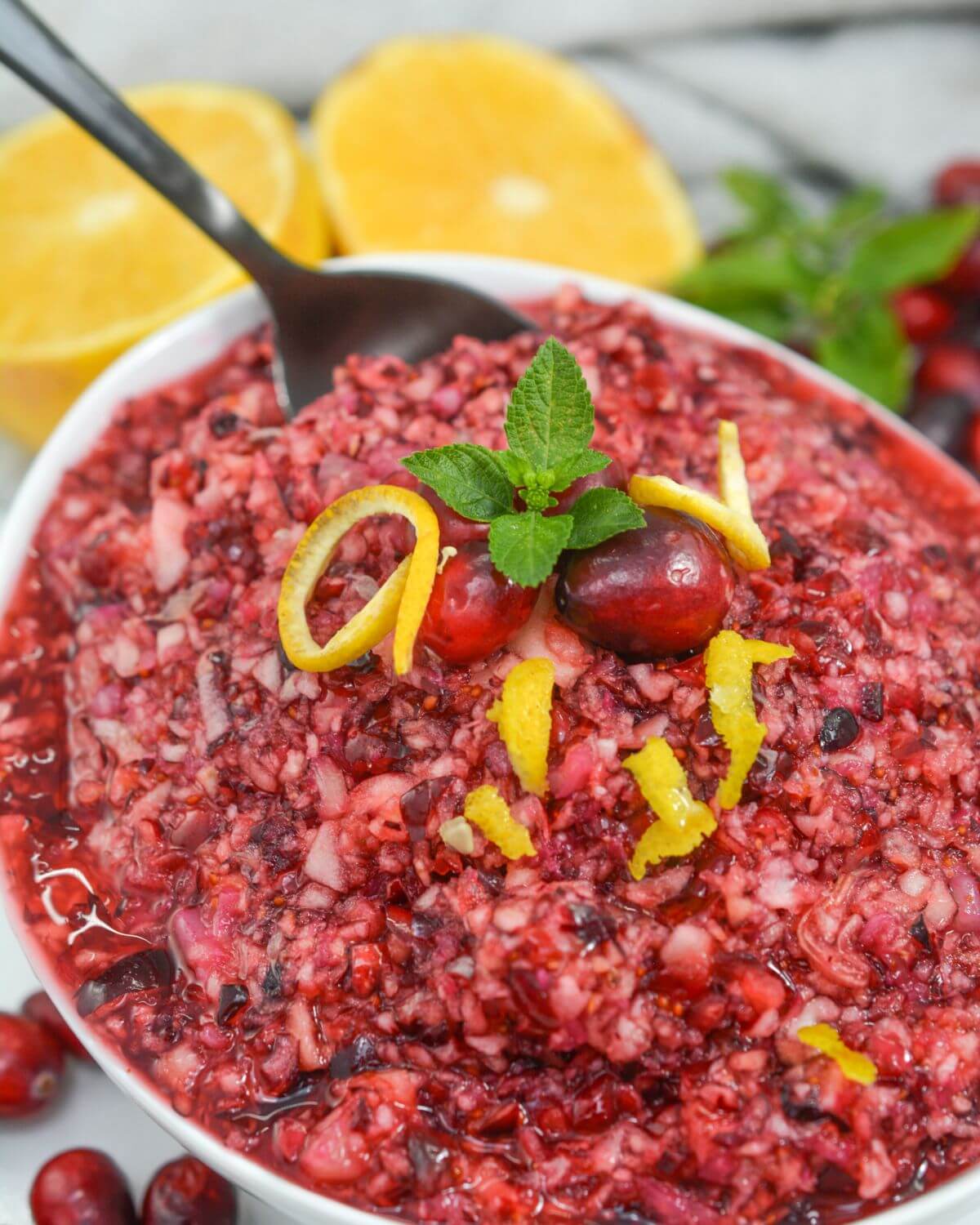 Fresh cranberry relish in a white bowl with orange peel, mint and cranberry garnish. 