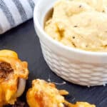 A small bowl of creamy garlic dip on a slate surface, perfectly paired with crunchy orange and brown snacks. The scene hints at a feast of Garlic Parmesan Chicken Wings, while a striped cloth adds a touch of warmth in the background.