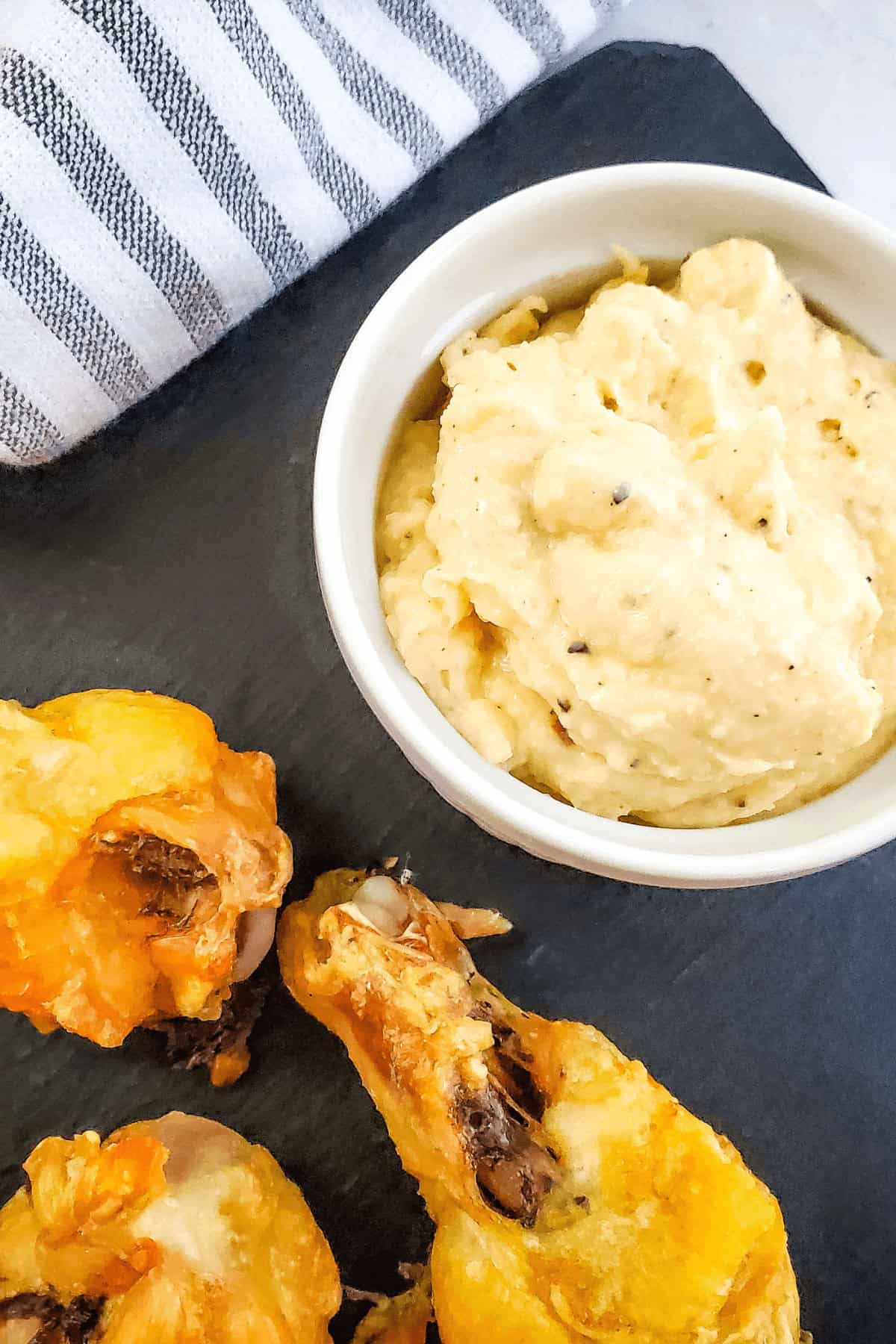 A bowl of creamy dip sits next to fried Garlic Parmesan Chicken Wings on a slate serving board, with a striped cloth nearby.