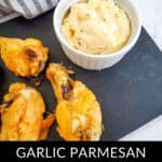 Garlic Parmesan chicken wings rest on a slate plate, perfectly golden and crispy, accompanied by a small dish of creamy sauce ready for dipping.