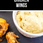A plate of tantalizing Garlic Parmesan chicken wings sits next to a bowl of creamy dip on a dark surface.