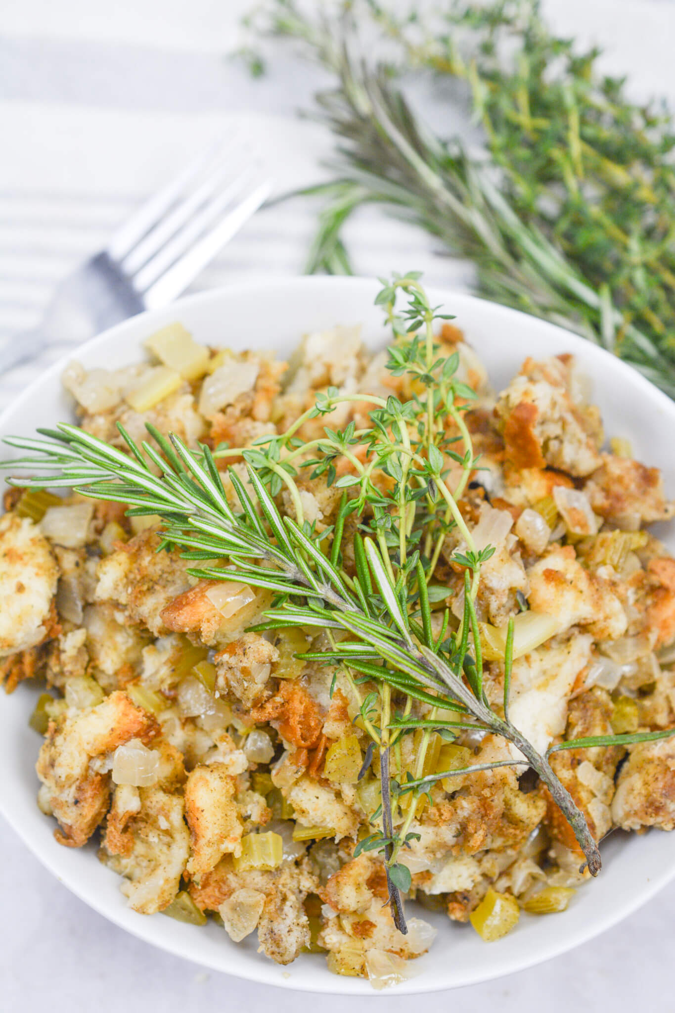 Sage and onion stuffing recipe in a white bowl with fresh herbs on top. 