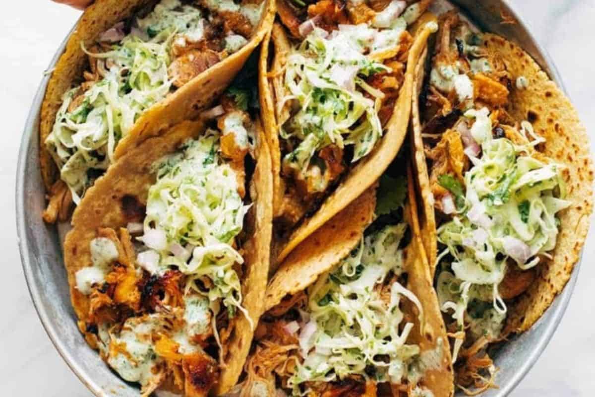 A plate of five soft tacos filled with shredded meat, chopped onions, lettuce, and a creamy green sauce—perfect as new mom freezer meals for quick and tasty dinners.