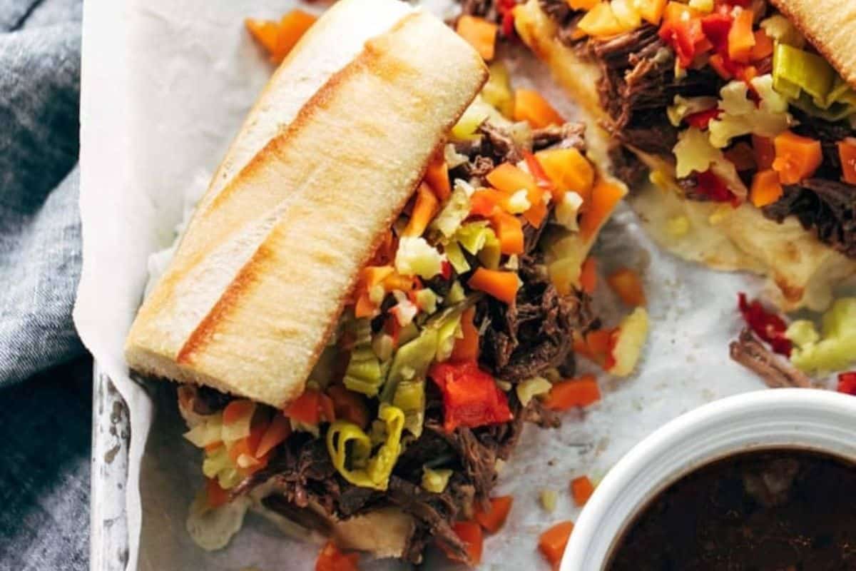 A perfect option for new mom freezer meals, this sandwich features shredded beef and pickled vegetables on a baguette, served with a bowl of dark dipping sauce.