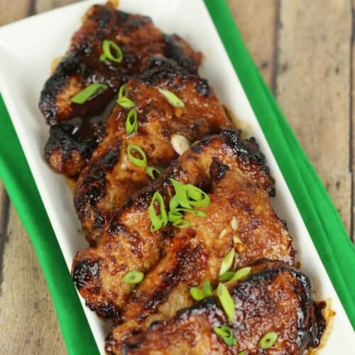 Glazed Korean pork chops on a rectangular white plate, garnished with sliced green onions.