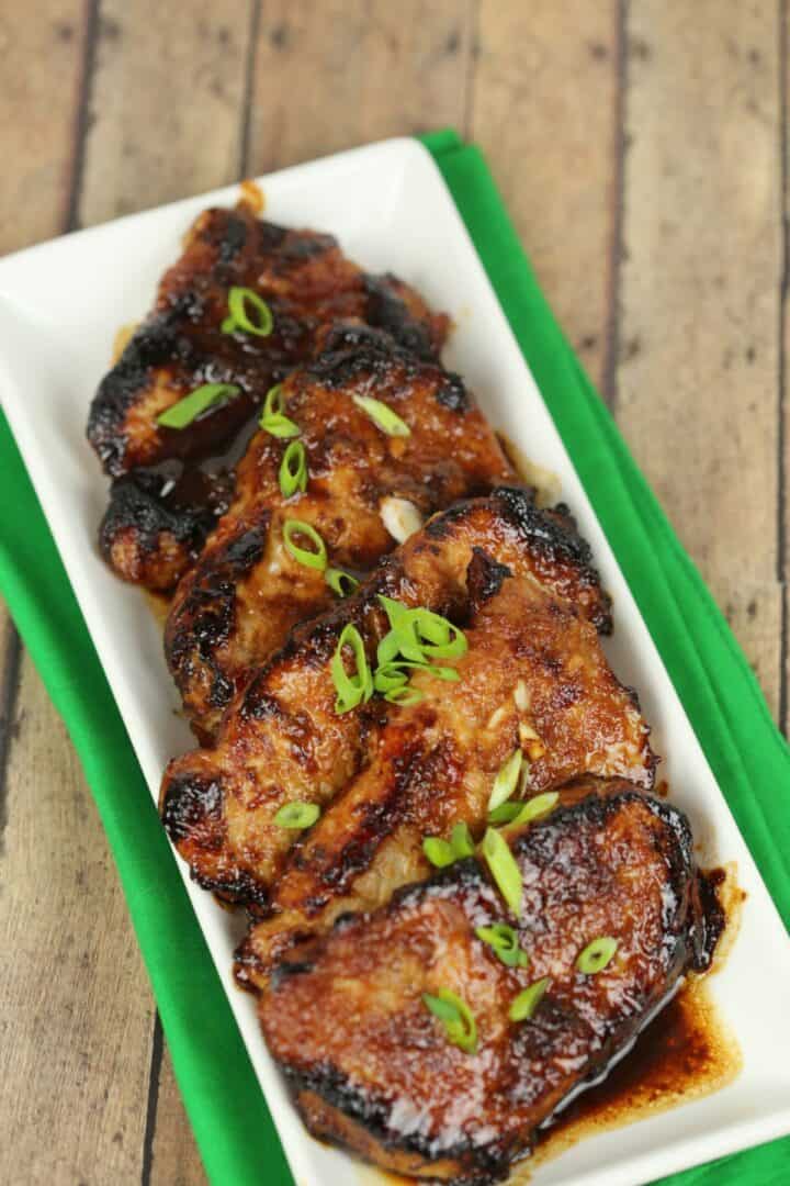 Glazed Korean pork chops on a rectangular white plate, garnished with sliced green onions.