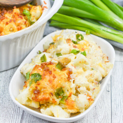 A dish of the Loaded Cheesy Cauliflower Bake with green onions on the side.