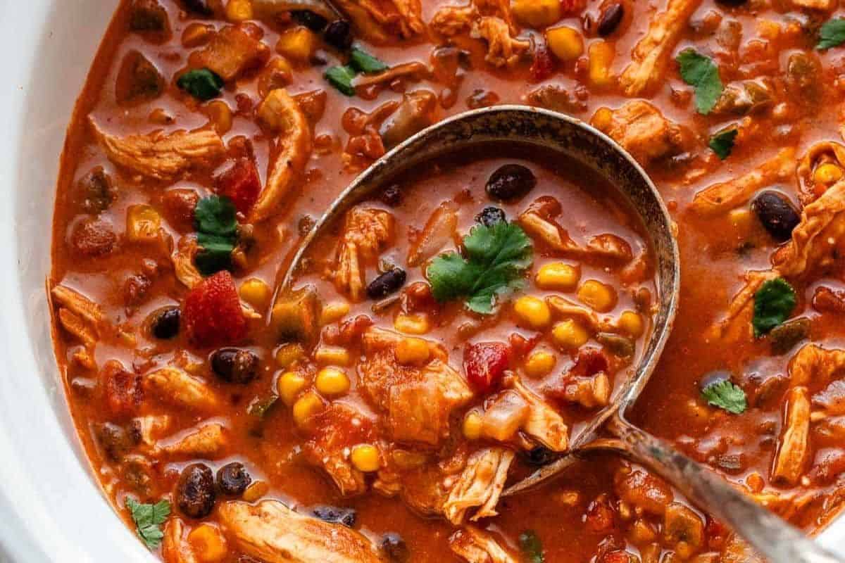 A ladle scoops a hearty chicken chili with black beans, corn, tomatoes, and cilantro—an ideal option for new mom freezer meals.