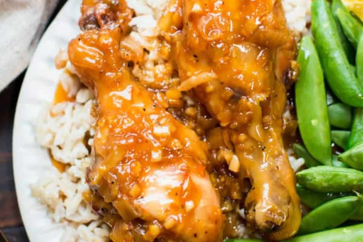 Two glazed chicken drumsticks on a bed of rice, served with green snap peas on a white plate—an easy and delicious option for new mom freezer meals.