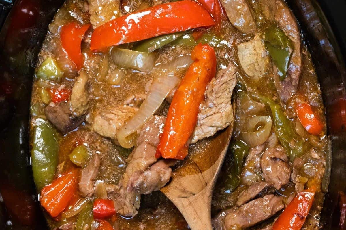 Hearty pepper steak with sliced red and green bell peppers, onions, and savory sauce, stirred with a wooden spoon—perfect for prepping as new mom freezer meals.