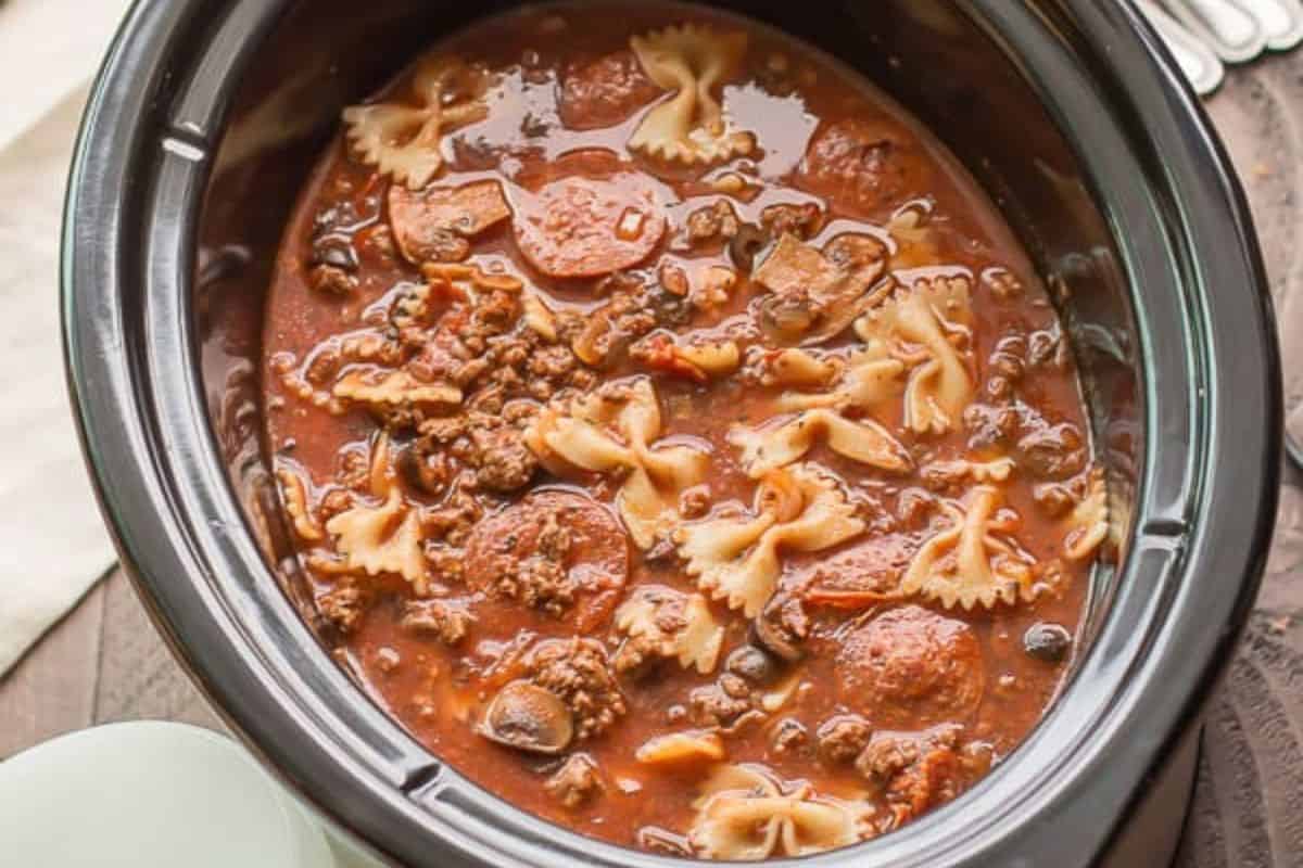 A crockpot filled with pasta, ground meat, sliced sausage, mushrooms, and tomato-based sauce—perfect for new mom freezer meals.