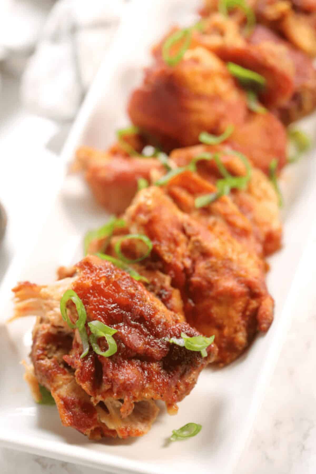 A close-up of sticky chicken pieces, perfectly fried and glistening with glaze, garnished with green onions on a white rectangular plate.