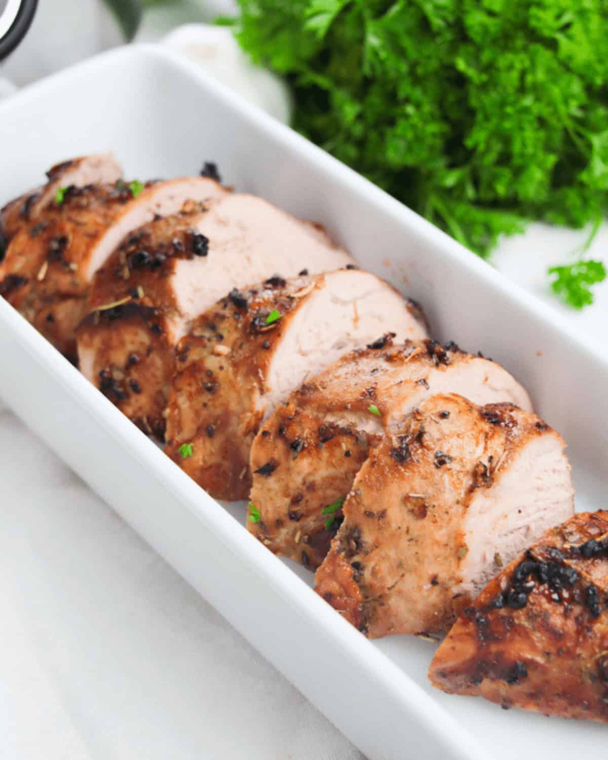 Grilled chicken breasts with parsley on a white plate.