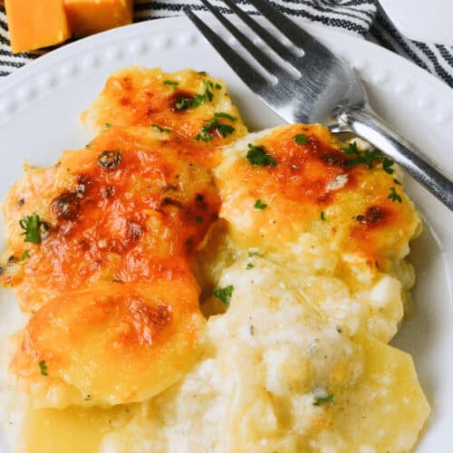 A plate of cheesy au gratin potatoes with Gruyere cheese, garnished with parsley, with a fork resting on the side.