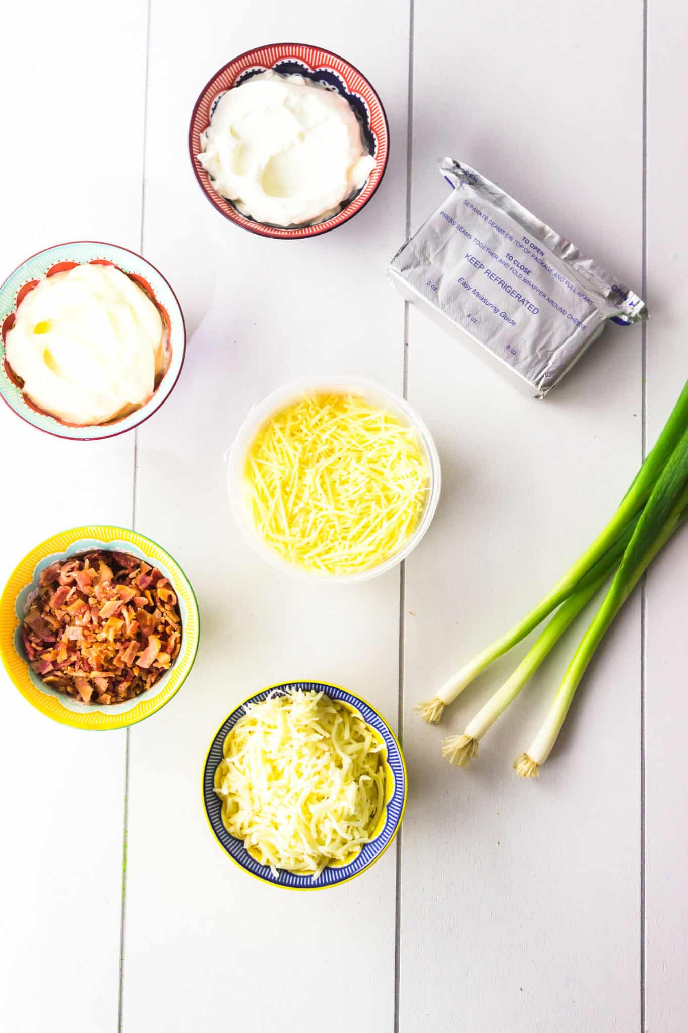 A white table with various bowls of cheese, green onions and cream cheese.