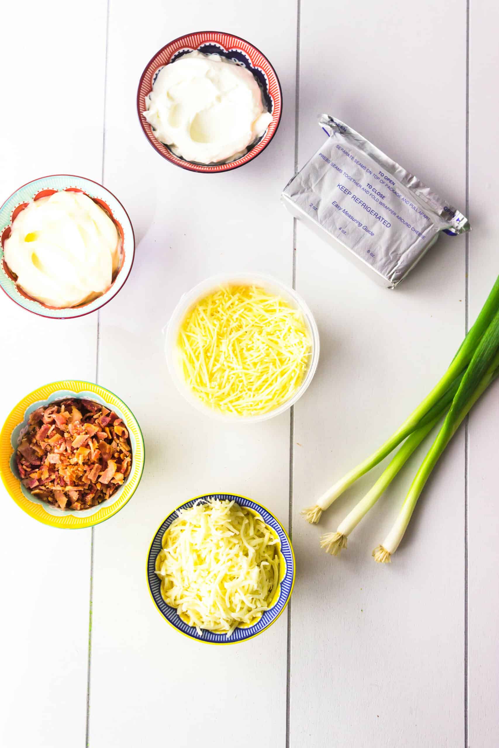 A white table with various bowls of cheese, green onions and cream cheese.