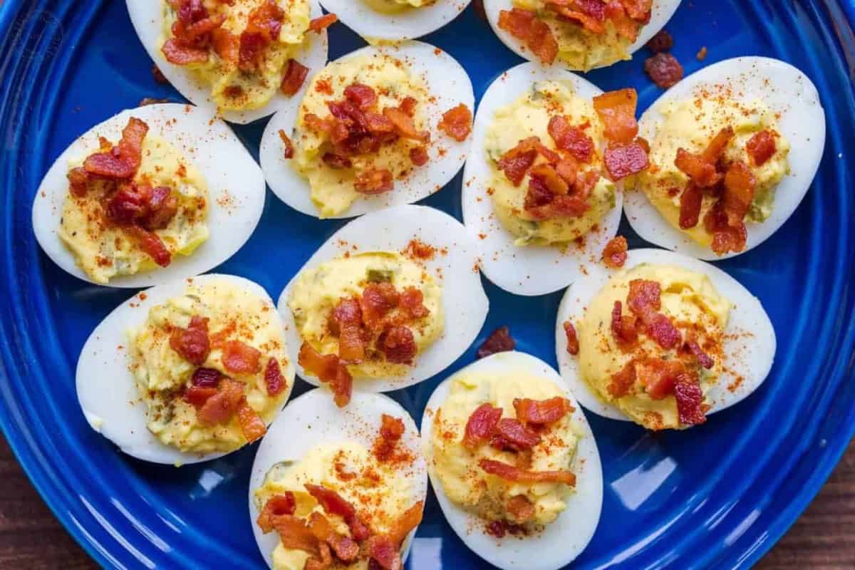 Deviled eggs topped with crumbled bacon and paprika, arranged on a blue plate.