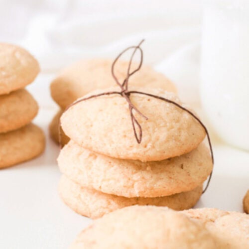 A stack of round snickerdoodle cookies made with cake mix is tied with twine, surrounded by more cookies. A glass bottle of milk sits invitingly in the background.