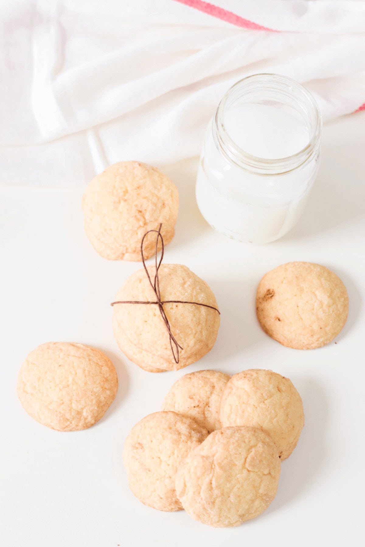 A delightful group of snickerdoodle cookies made with cake mix is arranged next to a jar of milk on a white surface, accompanied by a white and red cloth nearby.