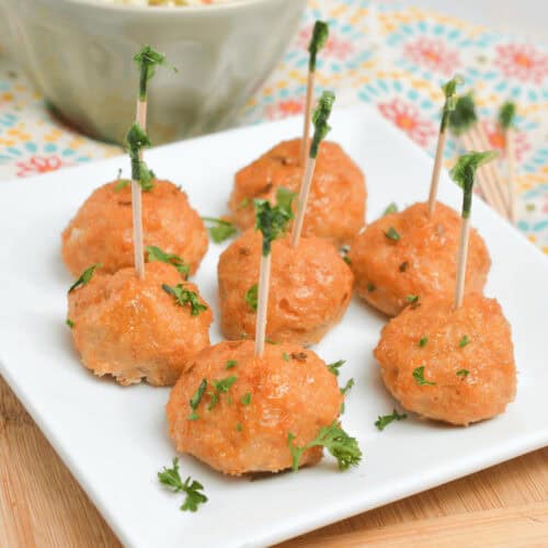 A plate of firecracker meatballs on toothpicks next to a bowl of coleslaw.