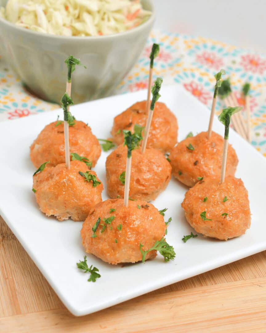 A plate of firecracker meatballs on toothpicks next to a bowl of coleslaw.