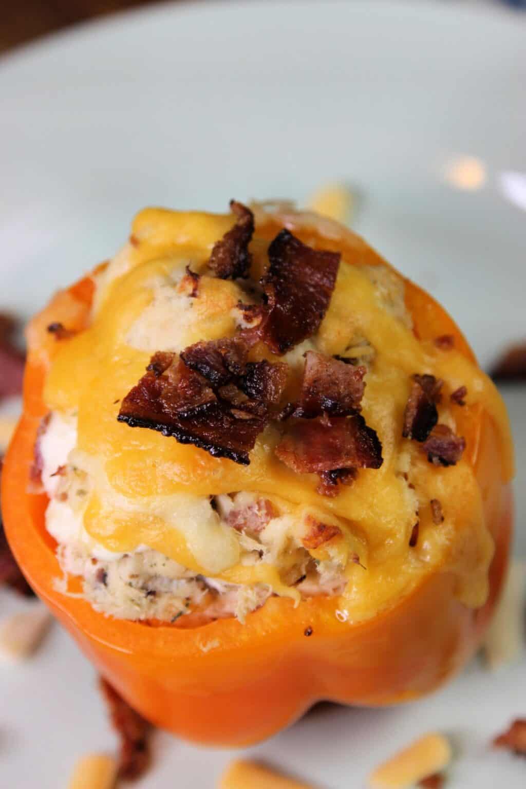 A Chicken Stuffed Bell Pepper topped with melted cheddar cheese and crumbled bacon is served on a white plate.