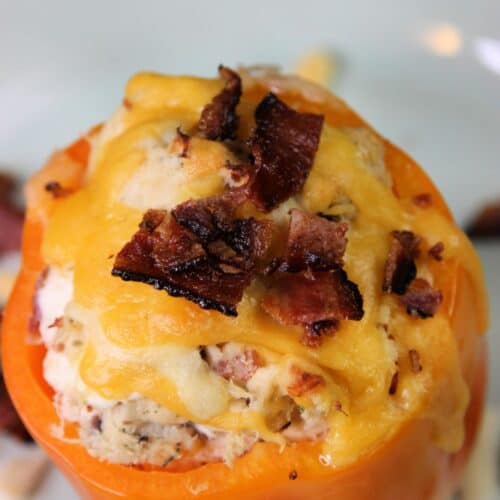A Chicken Stuffed Bell Pepper topped with melted cheddar cheese and crumbled bacon is served on a white plate.