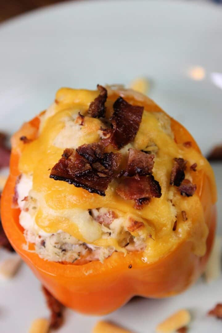 A Chicken Stuffed Bell Pepper topped with melted cheddar cheese and crumbled bacon is served on a white plate.