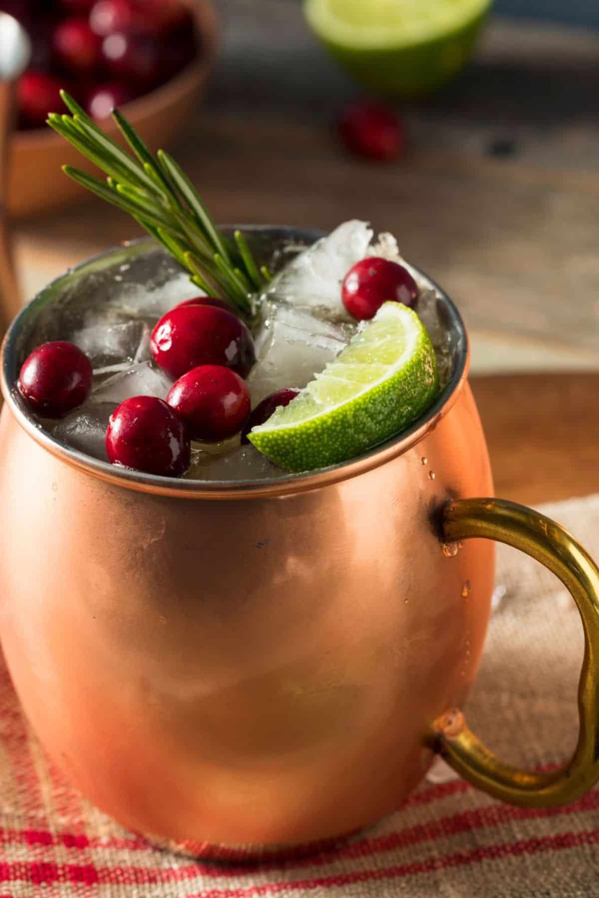 A copper mug filled with ice, cranberries, a lime for the holiday drink.