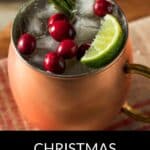 A festive copper mug filled with ice, cranberries, a lime wedge, and a rosemary sprig captures the holiday spirit of the Christmas Moscow Mule.