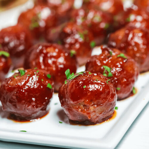 Sweet and spicy glazed meatballs garnished with parsley on a white plate.