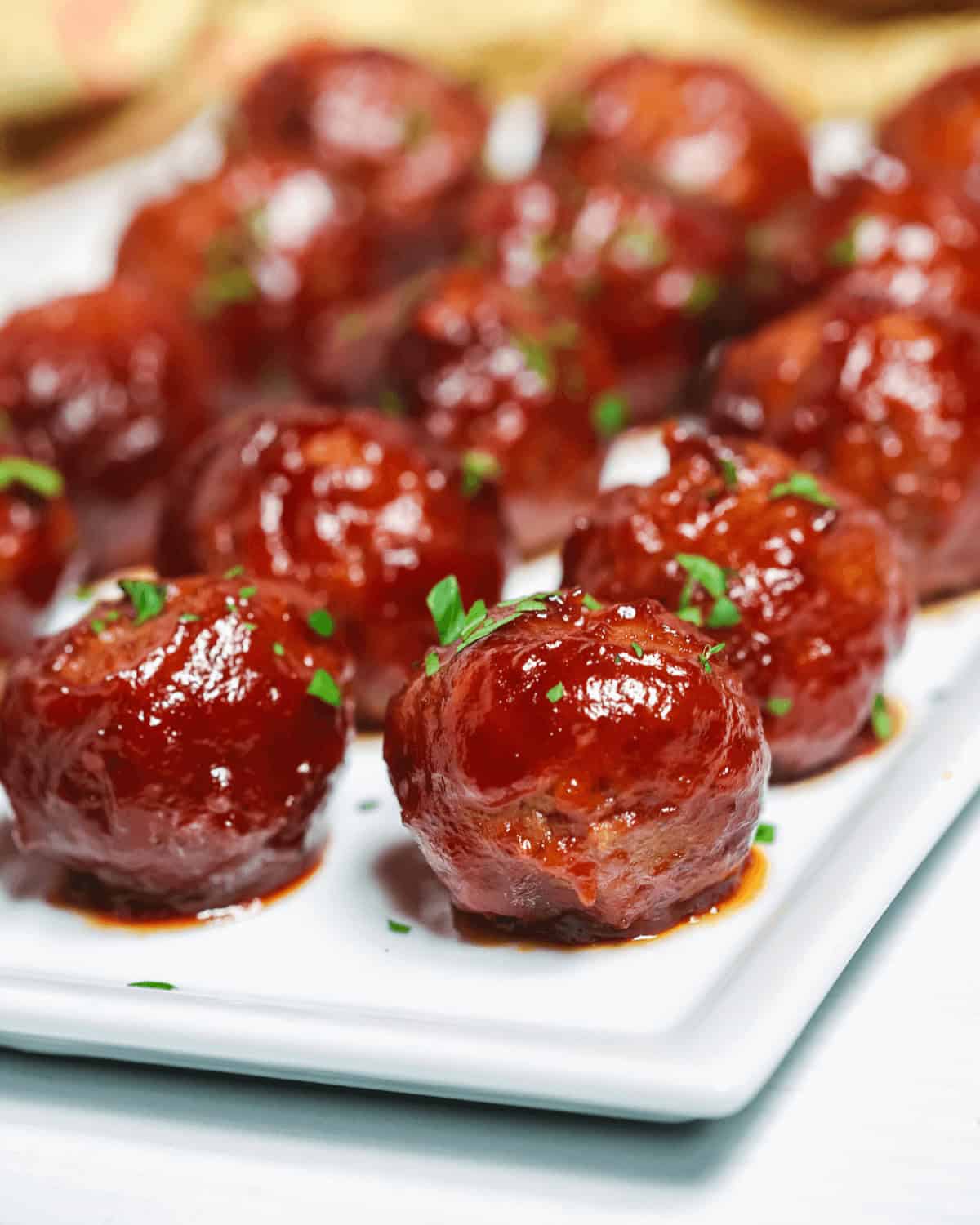 Sweet and spicy glazed meatballs garnished with parsley on a white plate.