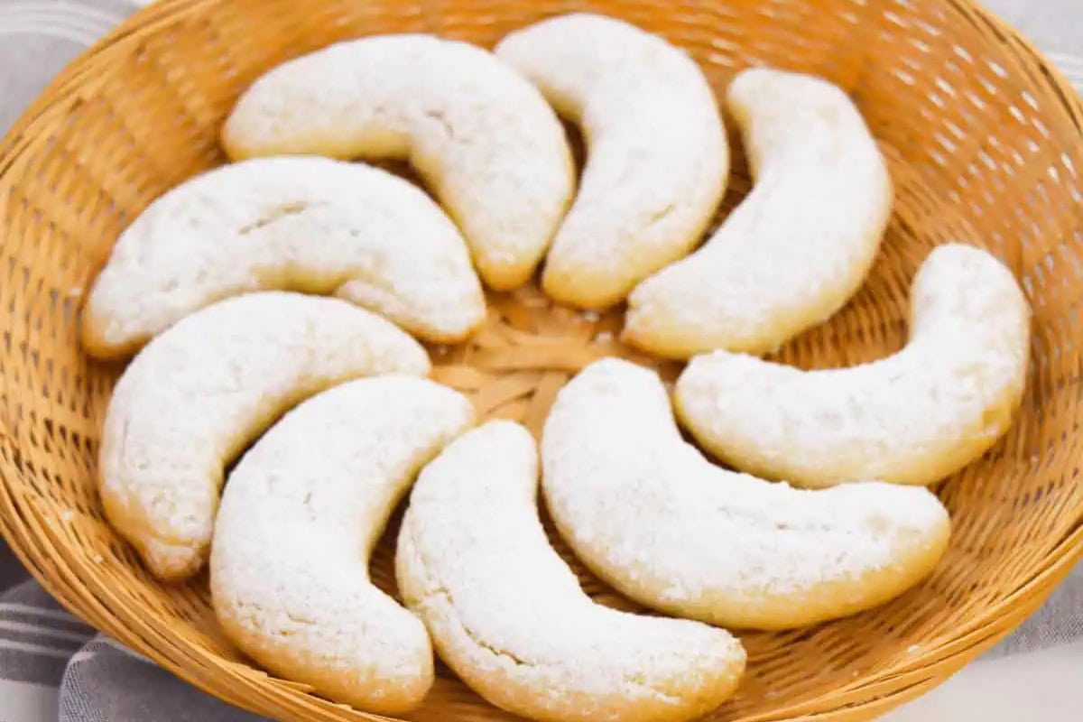 A wicker basket holds crescent-shaped almond cookies dusted with powdered sugar, arranged in a circular pattern—a delightful example of traditional Russian Christmas food.