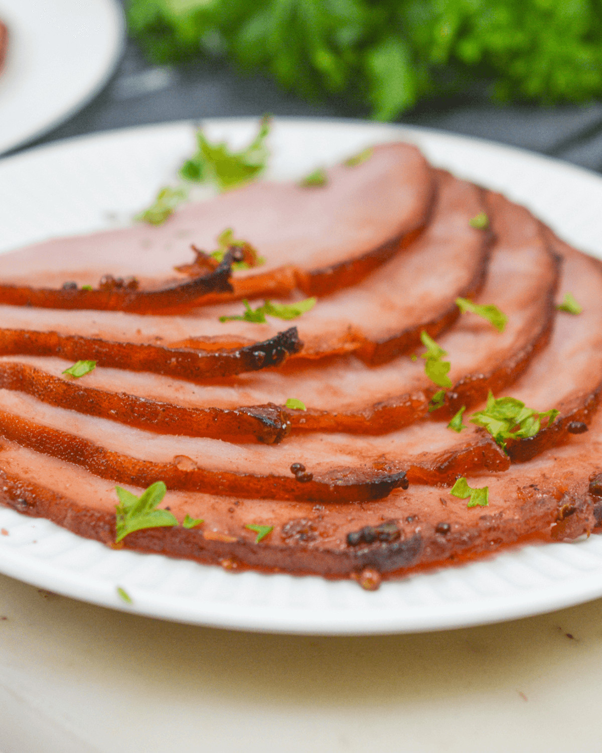 Sliced air fryer ham garnished with parsley on a white plate.