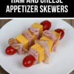 A delightful plate of appetizer skewers featuring cubes of cheddar cheese, rolled ham, and cherry tomatoes arranged on a wooden table.