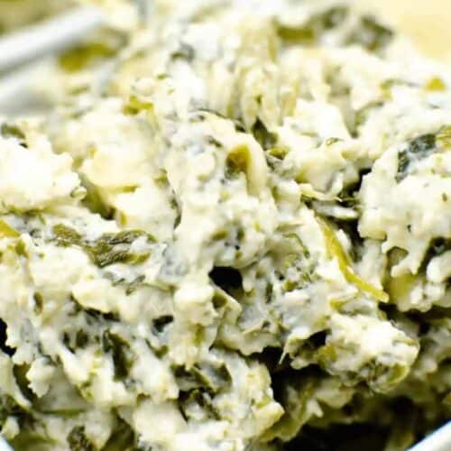 Close-up of a creamy spinach artichoke dip in a bowl, with vibrant green spinach and artichoke chunks harmoniously swirling into a velvety white base. This slow cooker dip is perfect for any gathering, offering a warm, comforting delight.