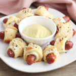Lil Smokies Pigs in a Blanket on a white plate with dip in the middle.