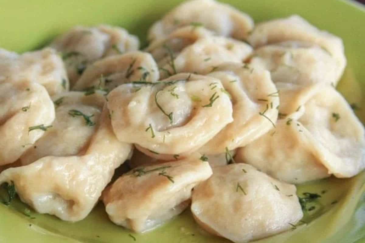 A light green plate of pelmeni garnished with chopped herbs and served on a green dish.