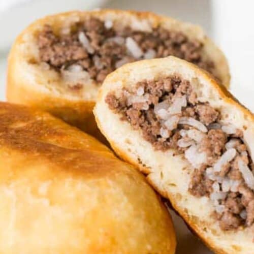 Close-up of two baked pastries filled with ground beef and rice, with one pastry cut open to show the hearty filling—a classic example of Russian food enjoyed at festive gatherings.